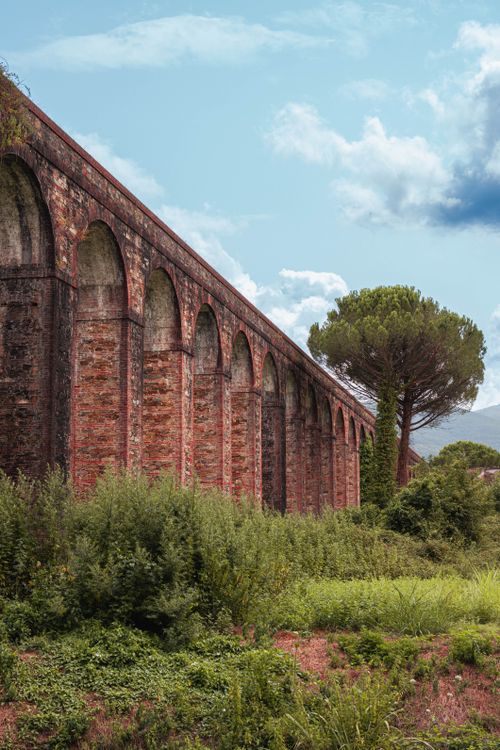 Free Beautiful historic aqueduct with arches set against a scenic Toscana landscape under a clear blue sky. Stock Photo