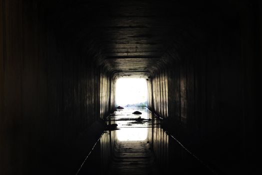 A dark tunnel leading to a bright light, creating a moody and dramatic silhouette.