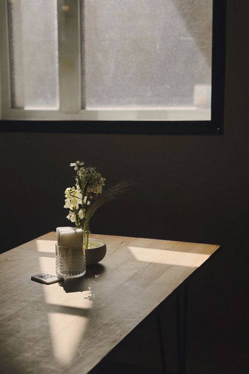 Free Sunlit table with a vase and remote control next to a window casting shadows. Stock Photo