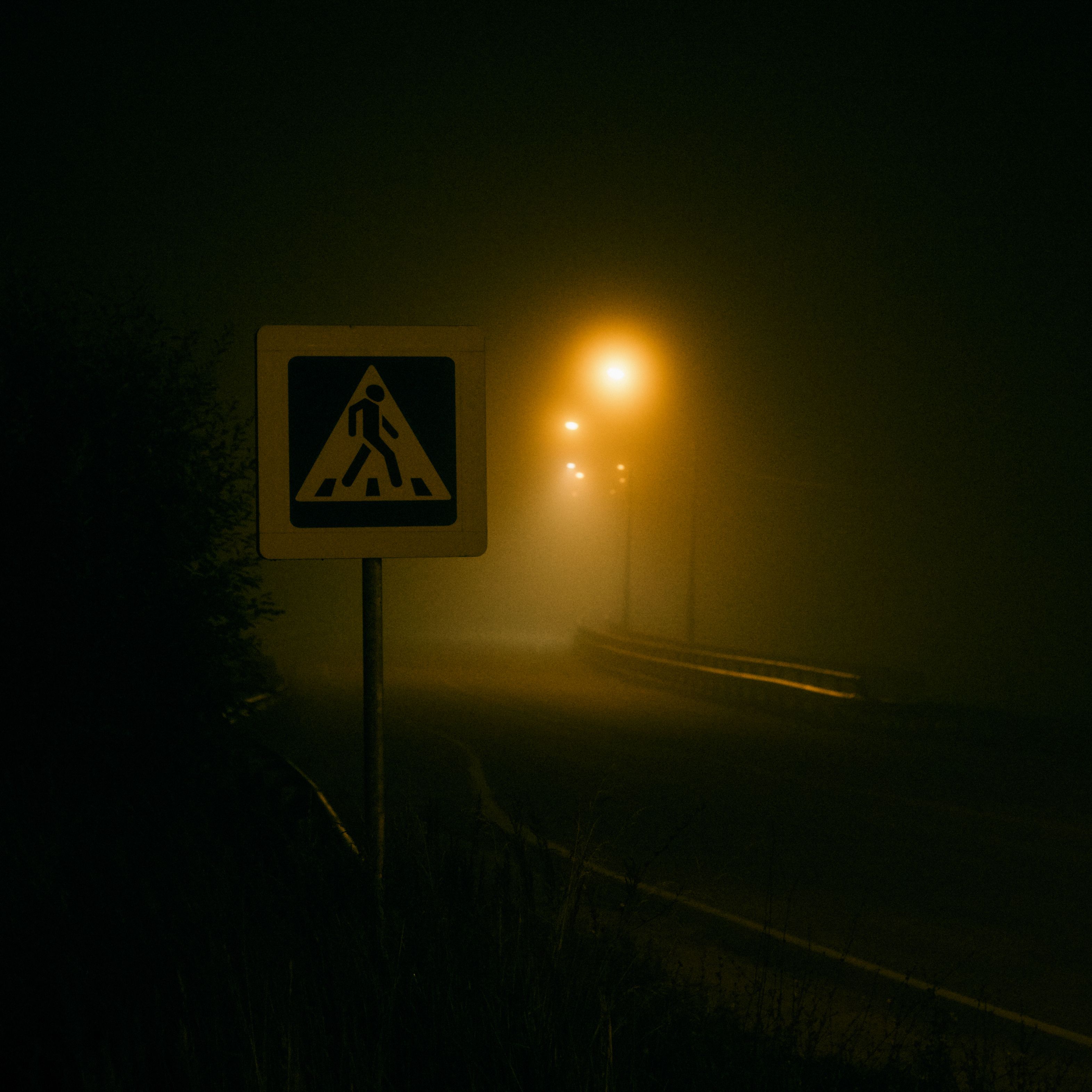 Mysterious foggy road illuminated by streetlights with a visible crosswalk sign.