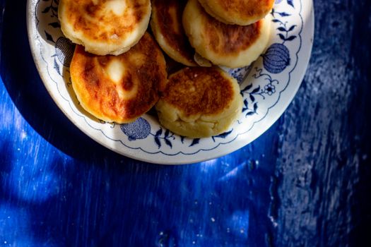 Appetizing fried cheese pancakes served on a decorative plate with blue background.
