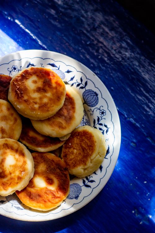 Free A plate of golden-brown syrniki served on a decorative plate against a vibrant blue background. Stock Photo