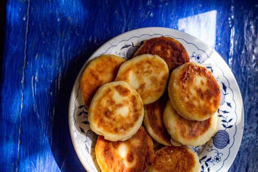 A plate of golden brown cheese pancakes with sunlight on a blue table.