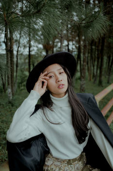 一位头戴软呢帽、身着西装外套的时髦女人，在宁静的森林中优雅地摆出姿势