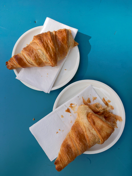 Top view of two fresh croissants on white plates with napkins set on a bright blue table.