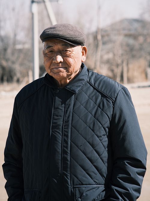 Free Portrait of an elderly man wearing a cap and quilted jacket outdoors in a rural setting. Stock Photo