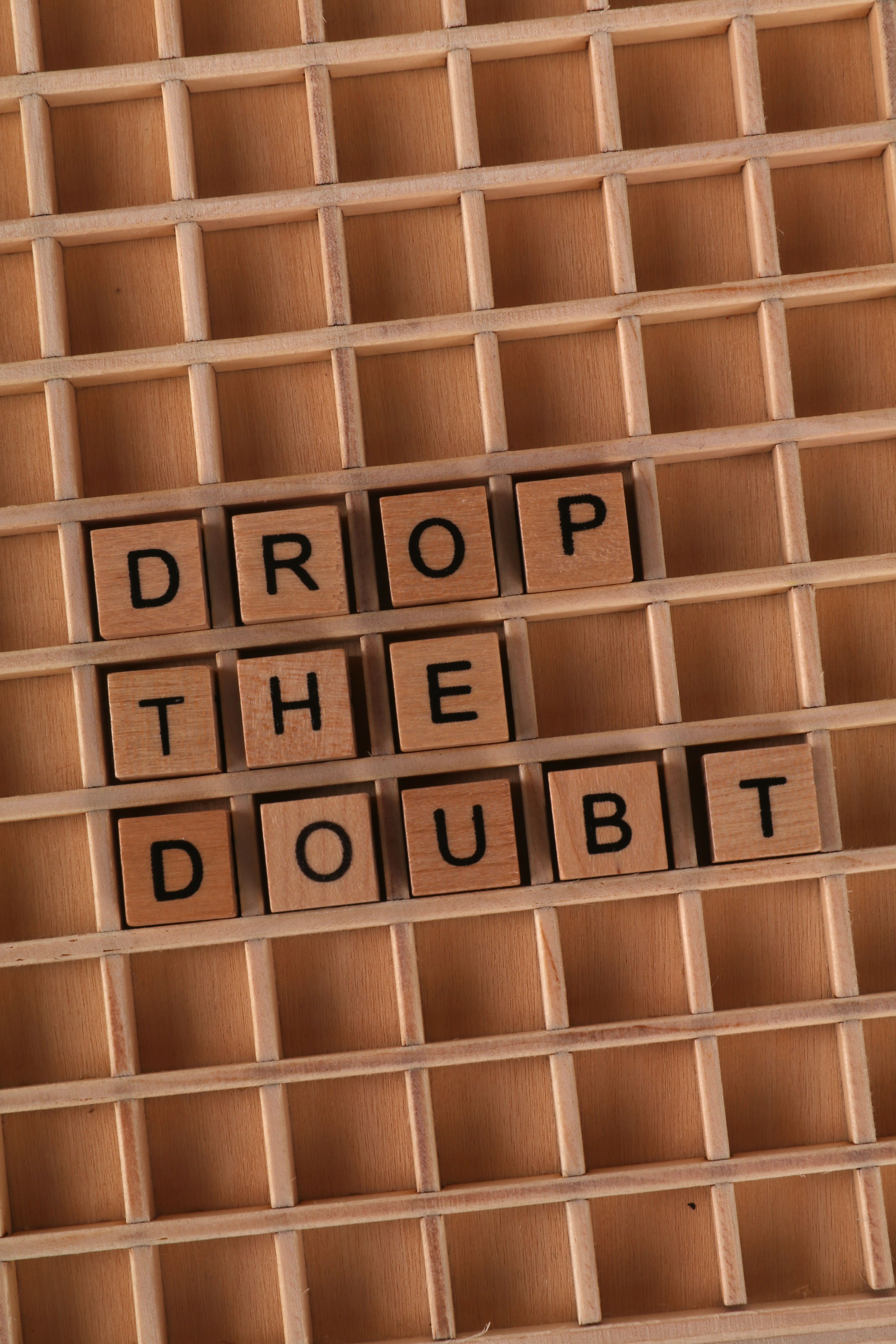 Wooden tiles spell 'Drop the Doubt' on a grid background, inspiring positivity.