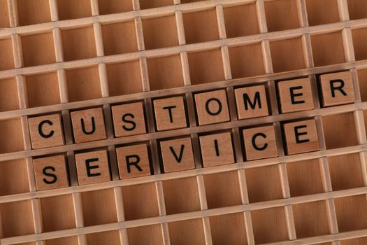 Wooden blocks forming the phrase 'Customer Service' placed inside a wooden grid, symbolizing support and assistance.