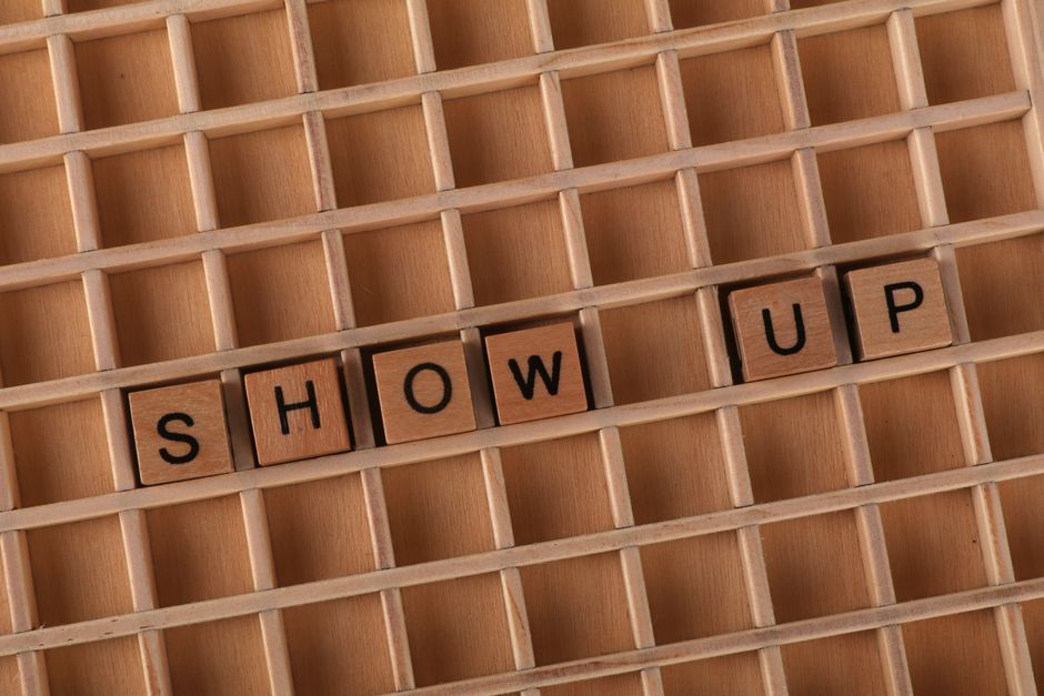モチベーションを高めるために、木製のグリッドの上に「Show Up」という文字を綴った木製の文字ブロックを平置きした写真。