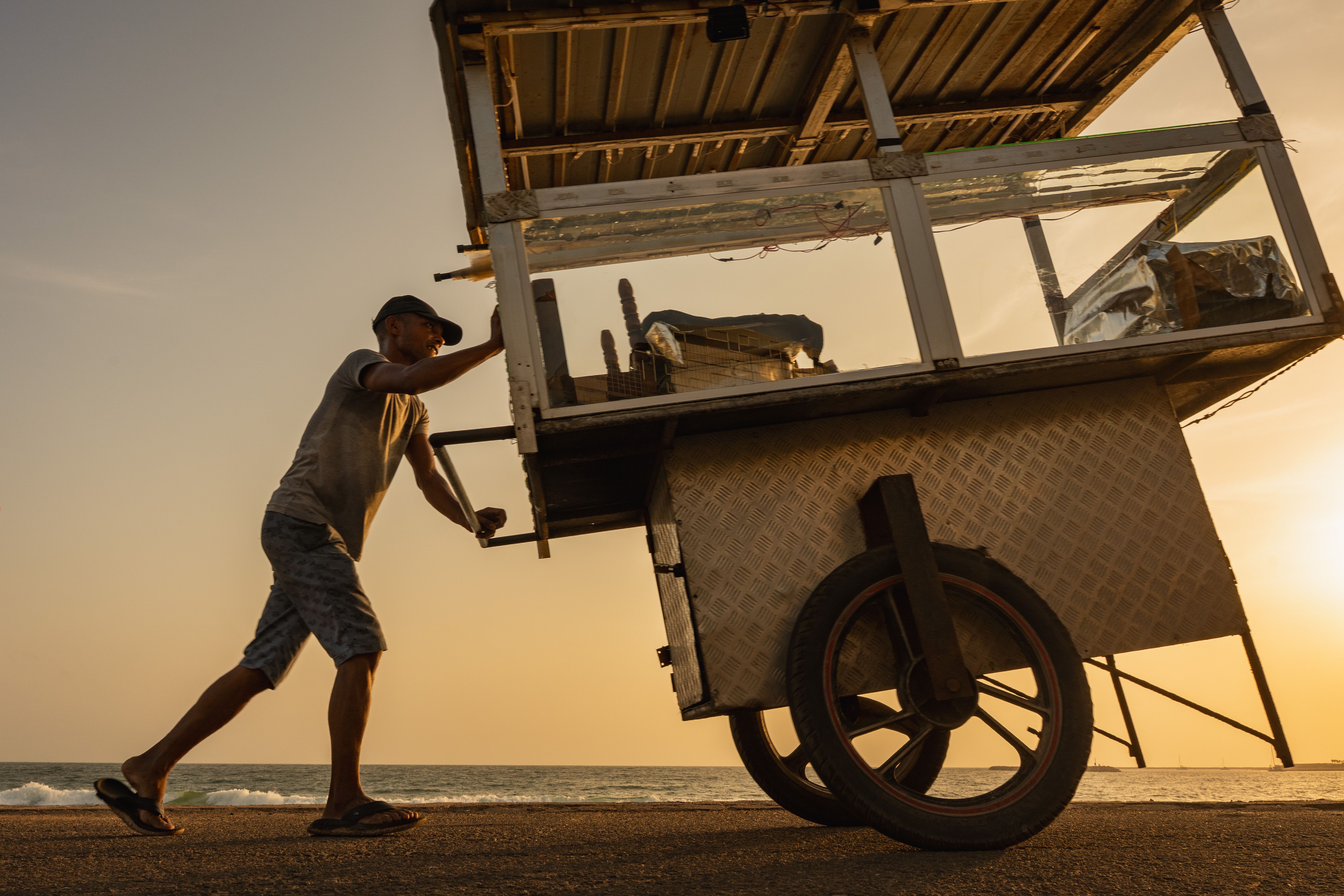A street vendor pushes a food cart along the beach in Colombo during a stunning sunset.