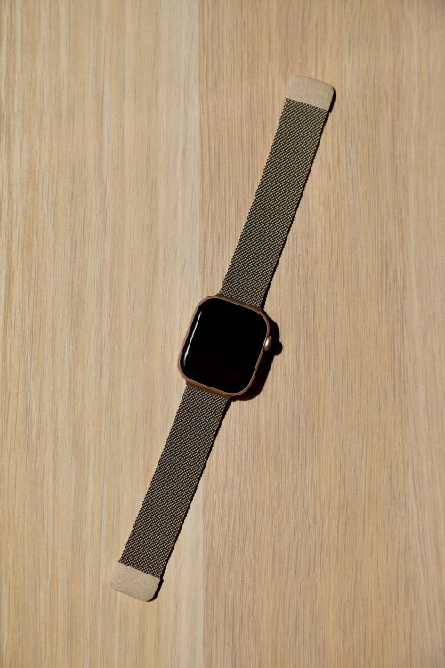 Free Flat lay of a modern smartwatch with a metal band on a wooden surface. Stock Photo