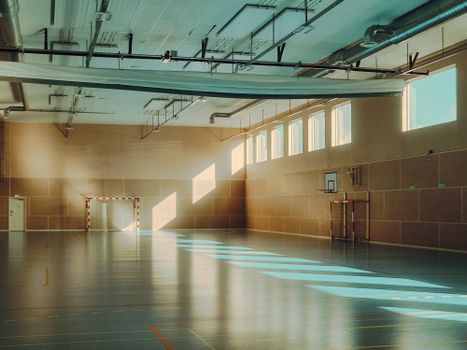 Empty gymnasium with sunlight streaming through windows highlighting sports gear.