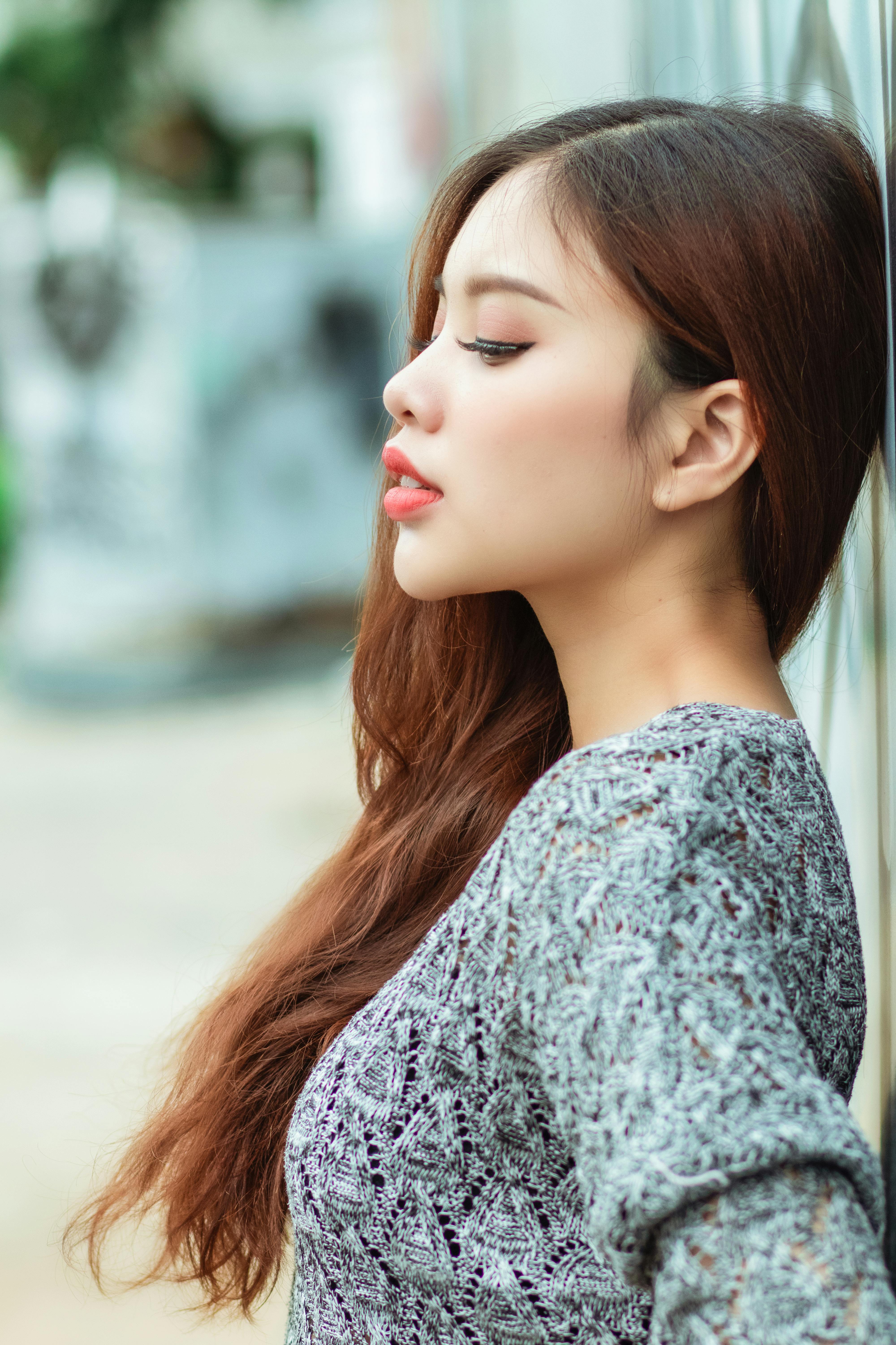 Profile of a fashionable young woman leaning against a wall, showcasing elegant style outdoors.