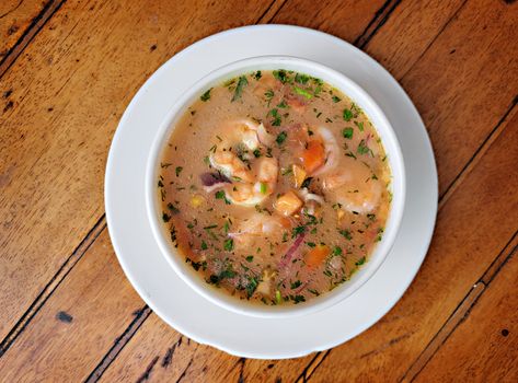 Appetizing shrimp stew with vegetables in a white bowl on a wooden table, showcasing Ecuadorian flavors.