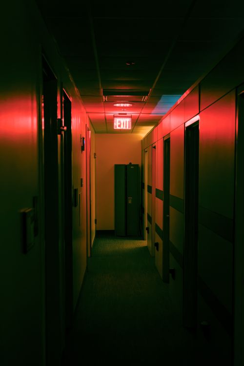 Free Dramatic corridor with a red exit sign casting warm tones in an office hallway. Stock Photo