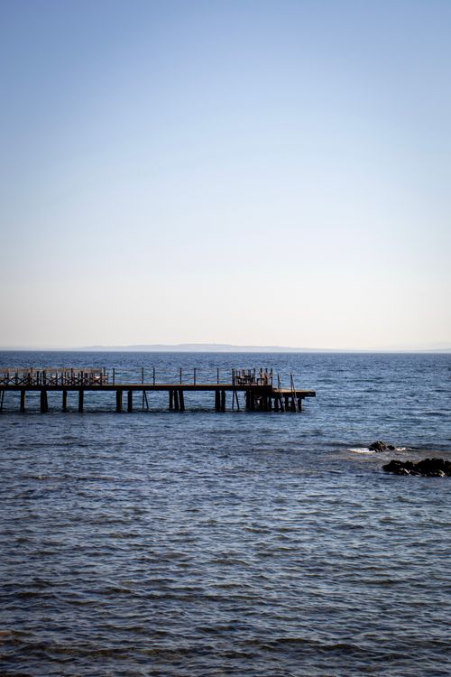 Free Serene view of an ocean pier extending into calm waters under a clear blue sky, perfect for relaxation themes. Stock Photo
