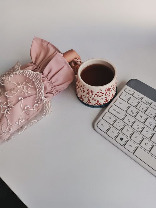 Free Elegant workspace with a cup of tea, embellished pink sleeve, and keyboard on a white desk. Stock Photo