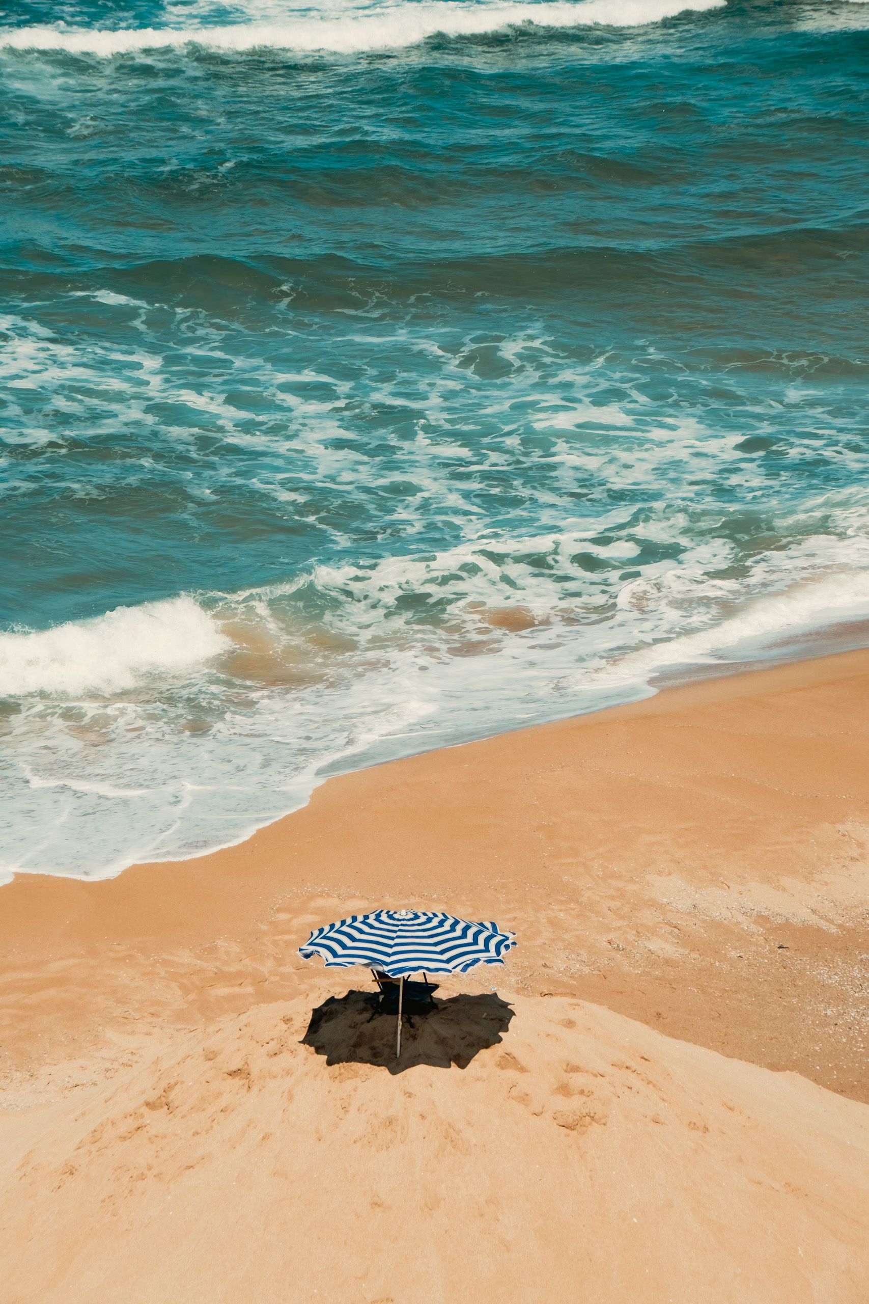 A lonely striped umbrella on a serene, sandy beach with gentle waves.