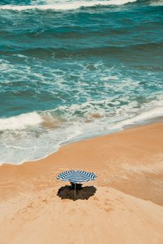 A lonely striped umbrella on a serene, sandy beach with gentle waves.