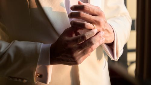 Free Close-up of a groom adjusting his ring, dressed in a light suit, bathed in sunlight. Stock Photo