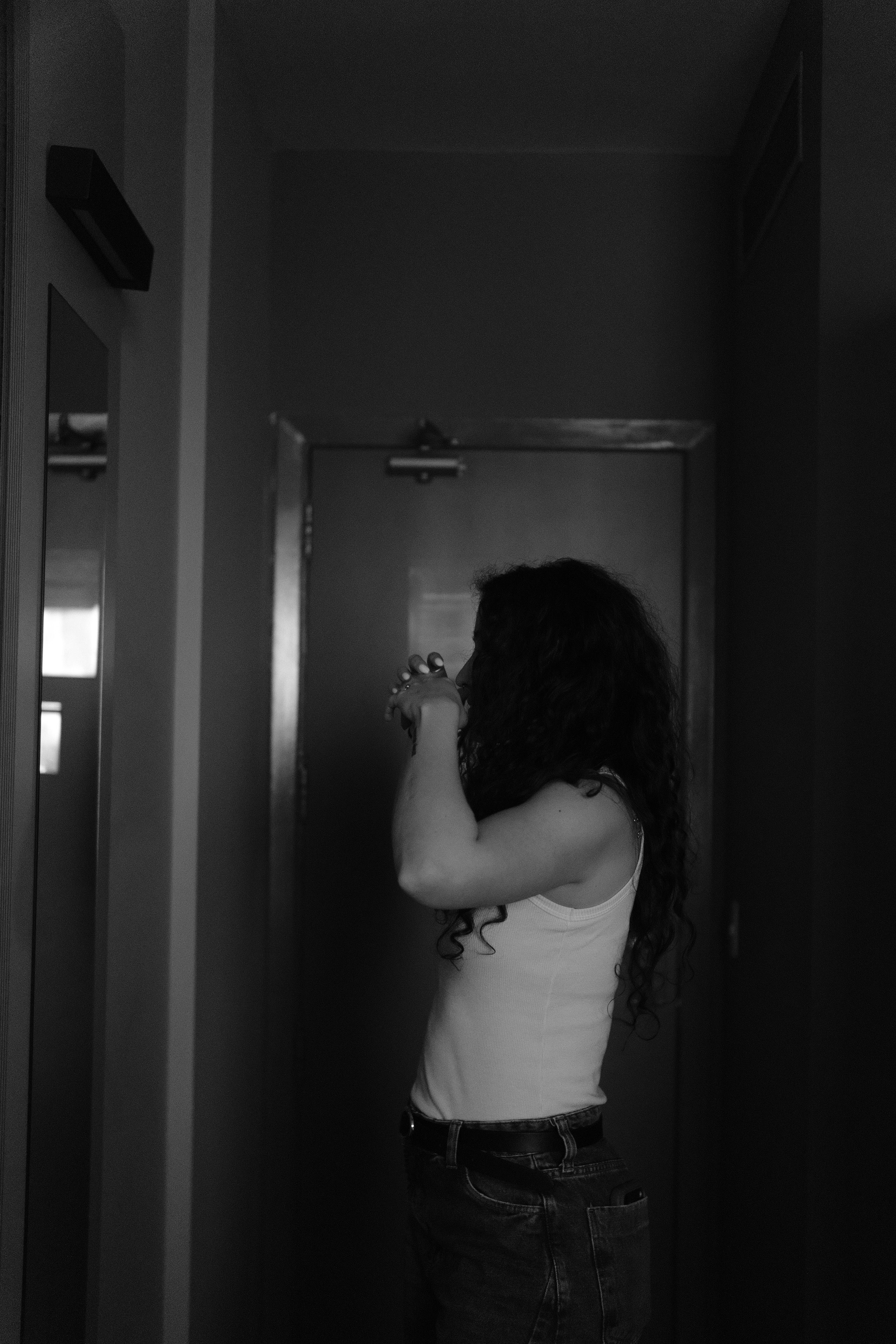 Black and white photo of a woman looking into a mirror indoors.