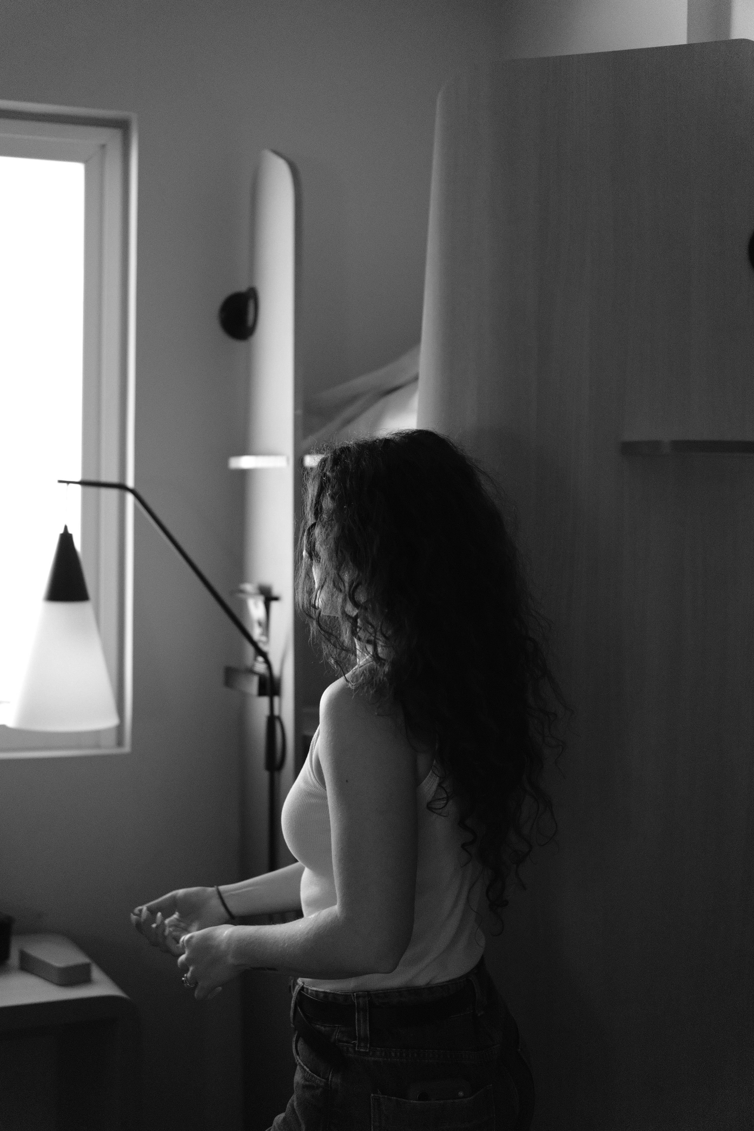 A woman stands by a window with soft light, creating a peaceful moment.