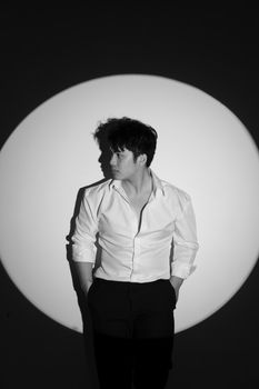 Black and white photo of a man in a spotlight, wearing a white shirt and dark pants.
