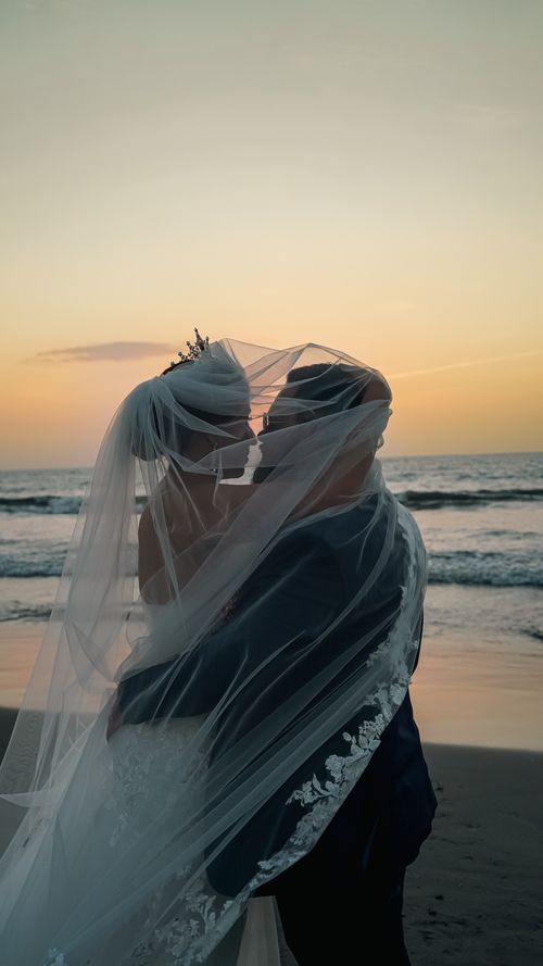 Free Bride and groom embrace on a beach during sunset, captured in a romantic silhouette. Stock Photo