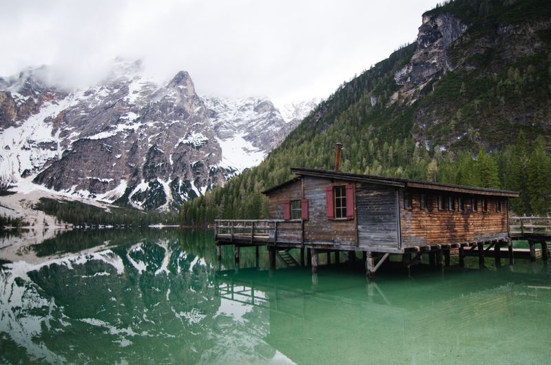 Cabana de lemn pe malul Lago di Braies cu munți înzăpeziți în fundal