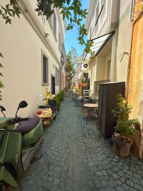 Free Picturesque alley in Balıkesir with scooters, potted plants, and outdoor seating on a sunny day. Stock Photo