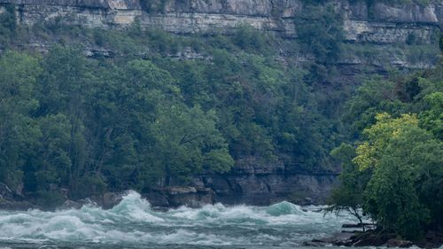 Free Dramatic river rapids flowing near a rocky cliff with dense forest. Stock Photo