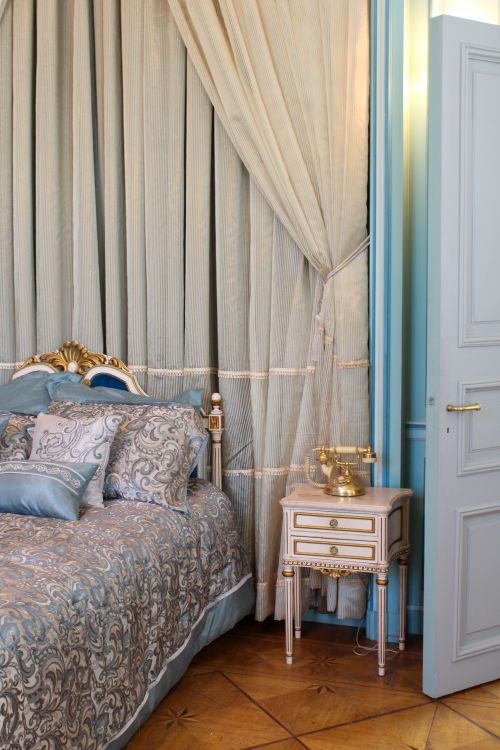 Free Luxurious bedroom featuring elegant bedding, vintage nightstand, and classic curtain design. Stock Photo