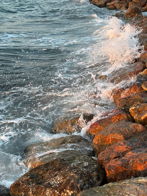 Free Dramatic waves crash against coastal rocks under a warm sunset light. Stock Photo