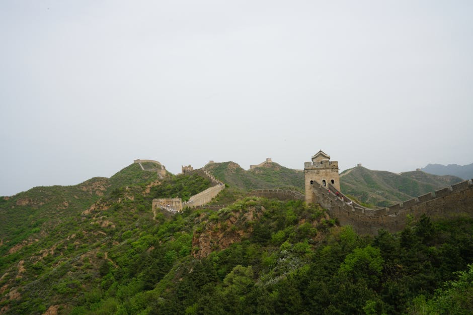 Panoramic view of the Great Wall of China weaving through lush green hills under a foggy sky.