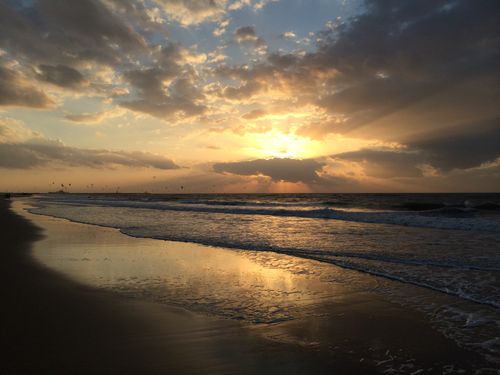Free A breathtaking sunset over a serene beach with dramatic cloud formations reflecting in the water. Stock Photo