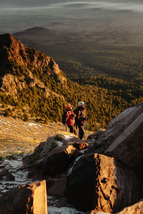 Free Two climbers hike a rocky trail with scenic mountain views at sunset. Stock Photo