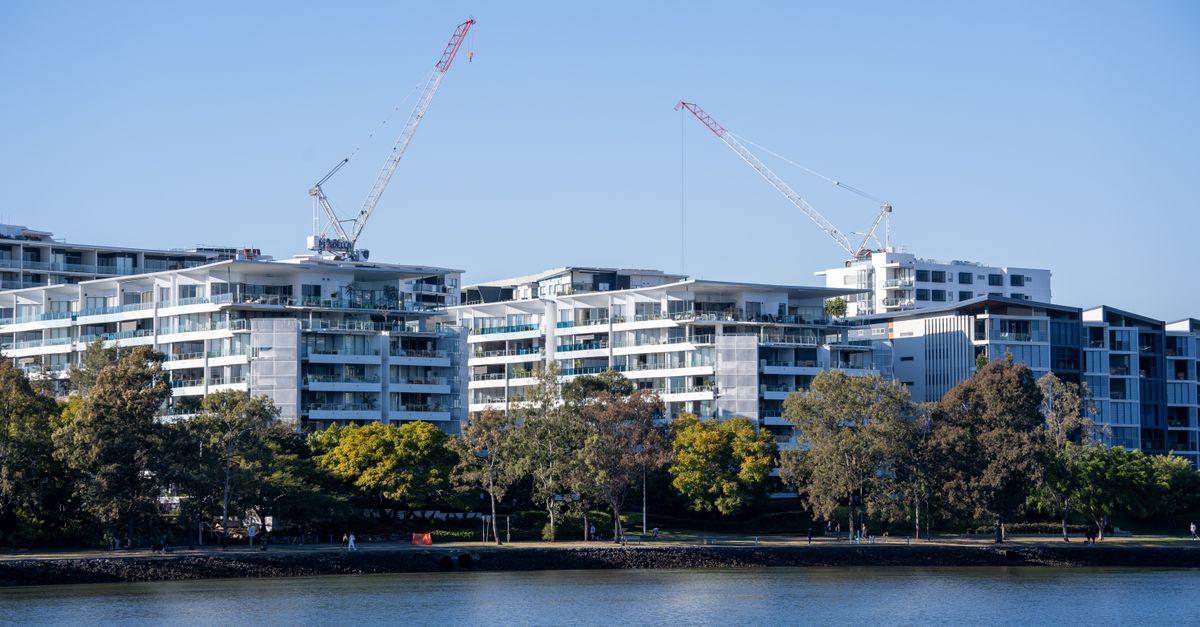 Luxurious riverside apartments under construction with cranes against a clear blue sky.