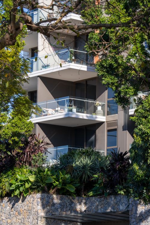 Free Contemporary apartment building with glass balconies surrounded by lush green foliage. Stock Photo