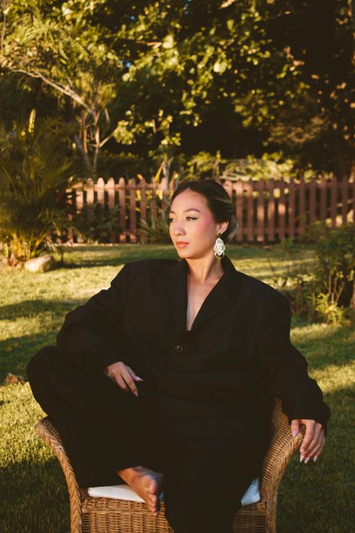 Free A woman in a black suit relaxing in a chair in a sunlit garden. Stock Photo