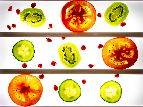Colorful slices of kiwi, tomato, and cucumber illuminated against a lightbox backdrop.
