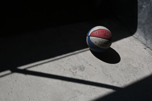 Moody shot of a basketball casting shadows on a concrete floor.