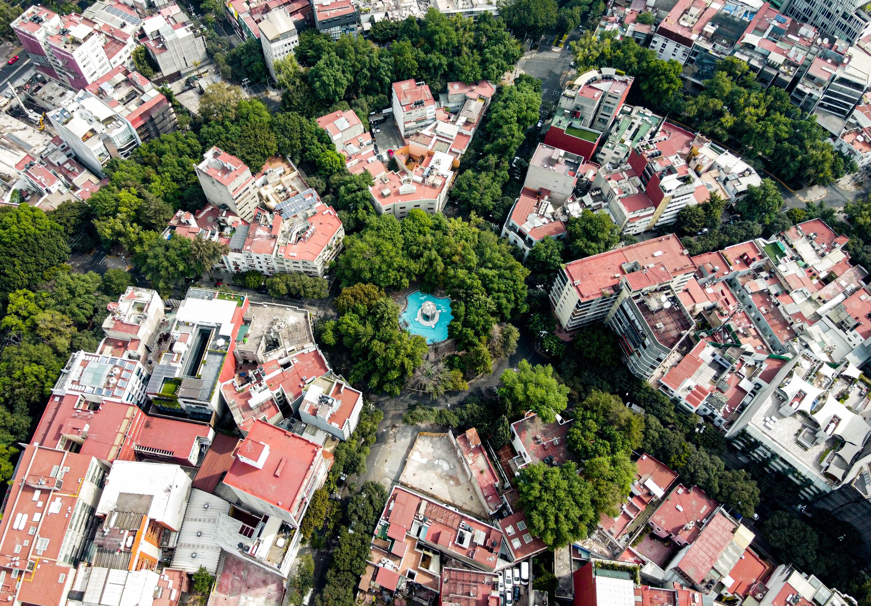 Aerial view of Mexico City's lush park surrounded by urban landscape and red-tiled rooftops.