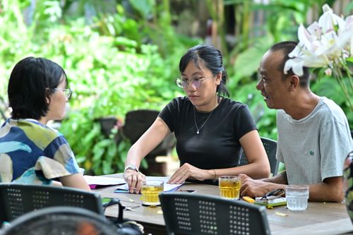 Free Group of adults engaged in discussion at a table in a lush garden setting, promoting teamwork and collaboration. Stock Photo
