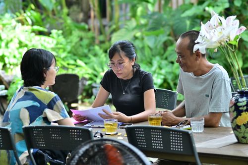 Free Three adults discussing documents over drinks in a green outdoor setting, emphasizing collaboration. Stock Photo