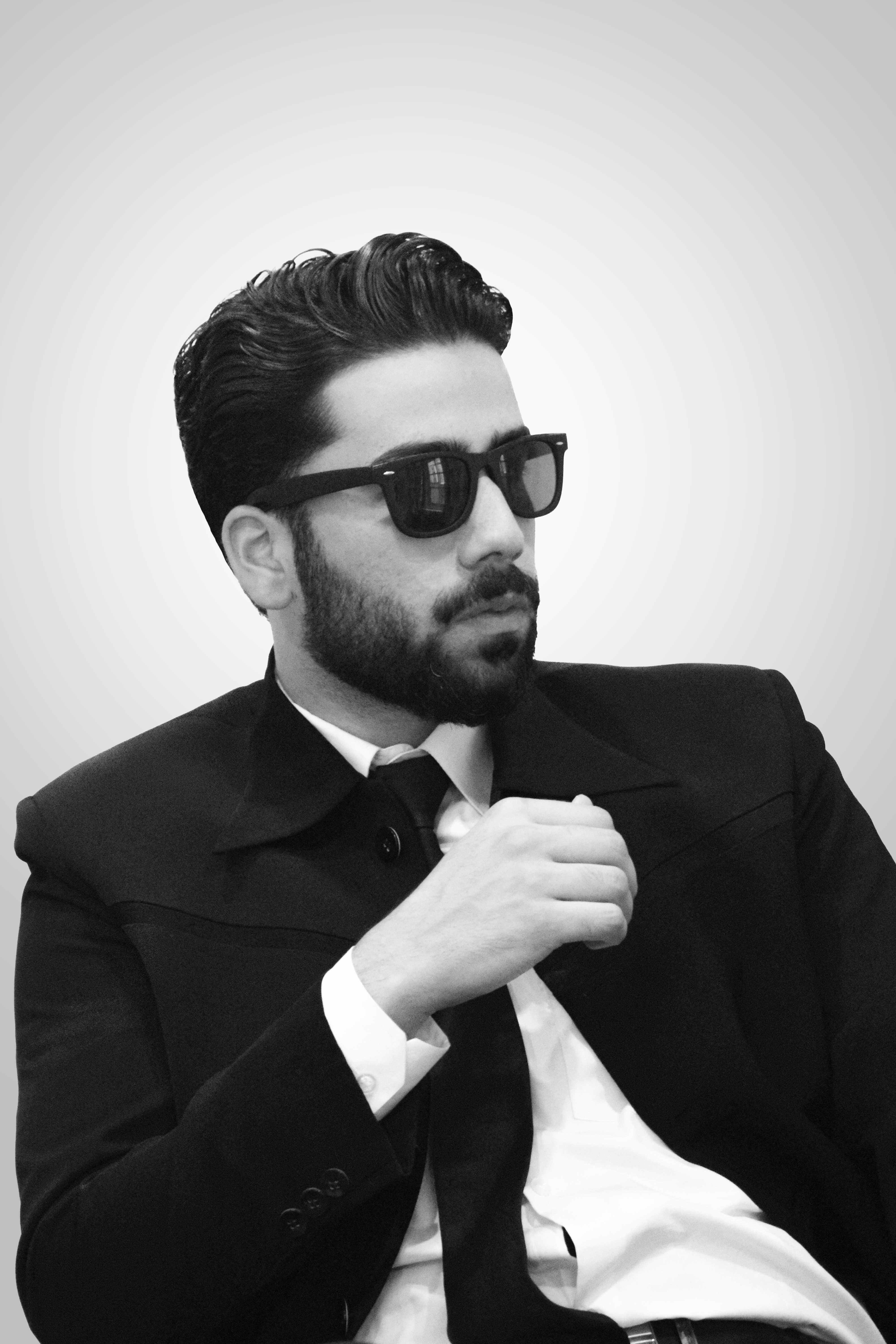 Black and white portrait of a stylish man in a suit and sunglasses, exuding confidence.