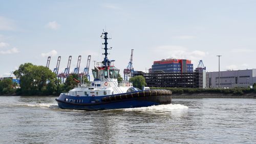 Free A tugboat cruises through the Hamburg harbour with cranes and a cityscape in the background. Stock Photo