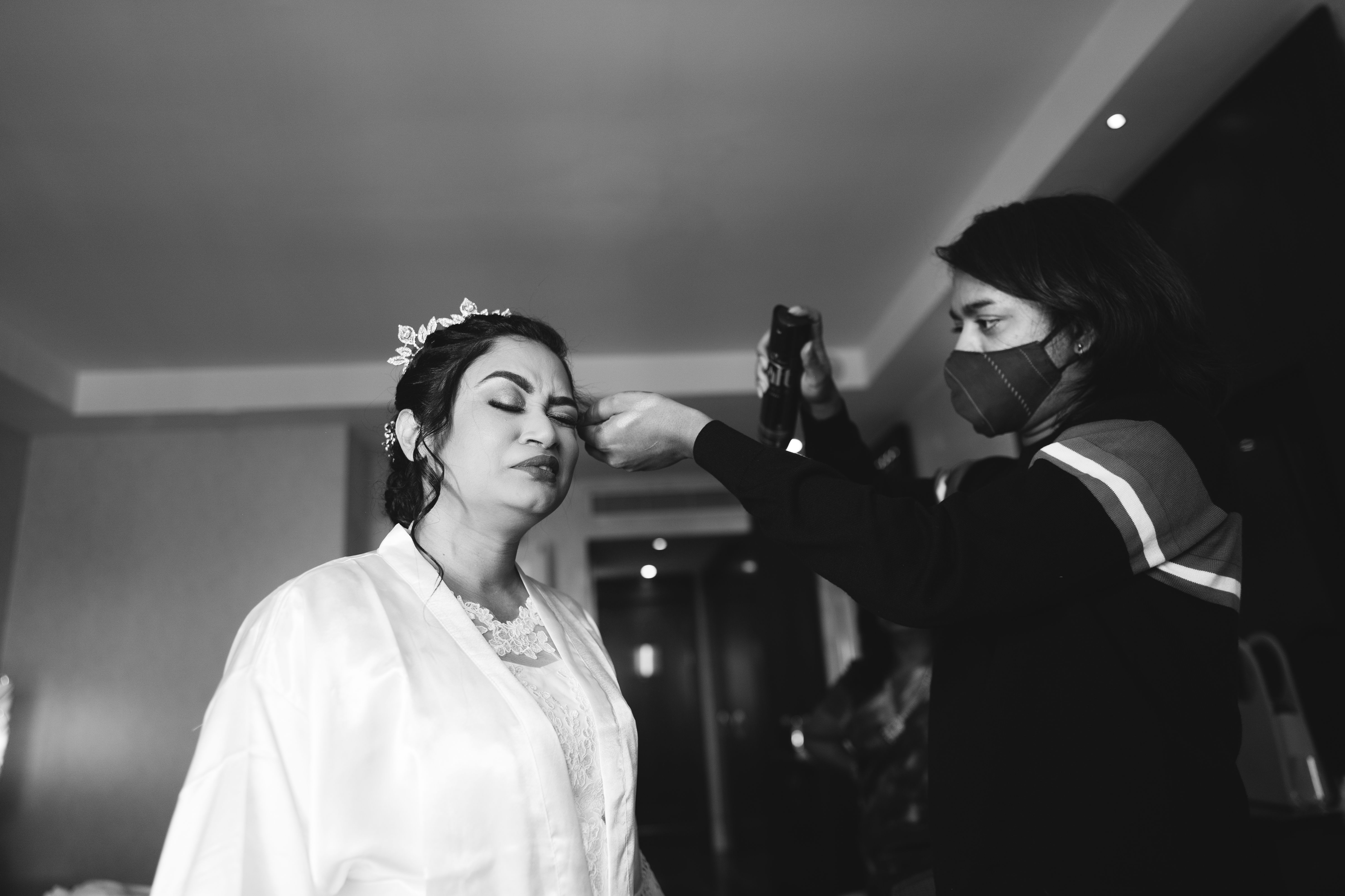 Bride getting makeup done indoors by a stylist wearing a mask.