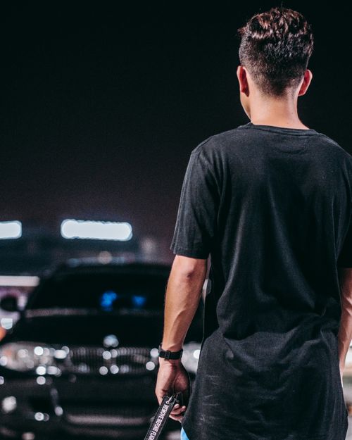 Free A man in casual wear standing near a parked car in a lot at night, viewed from behind. Stock Photo