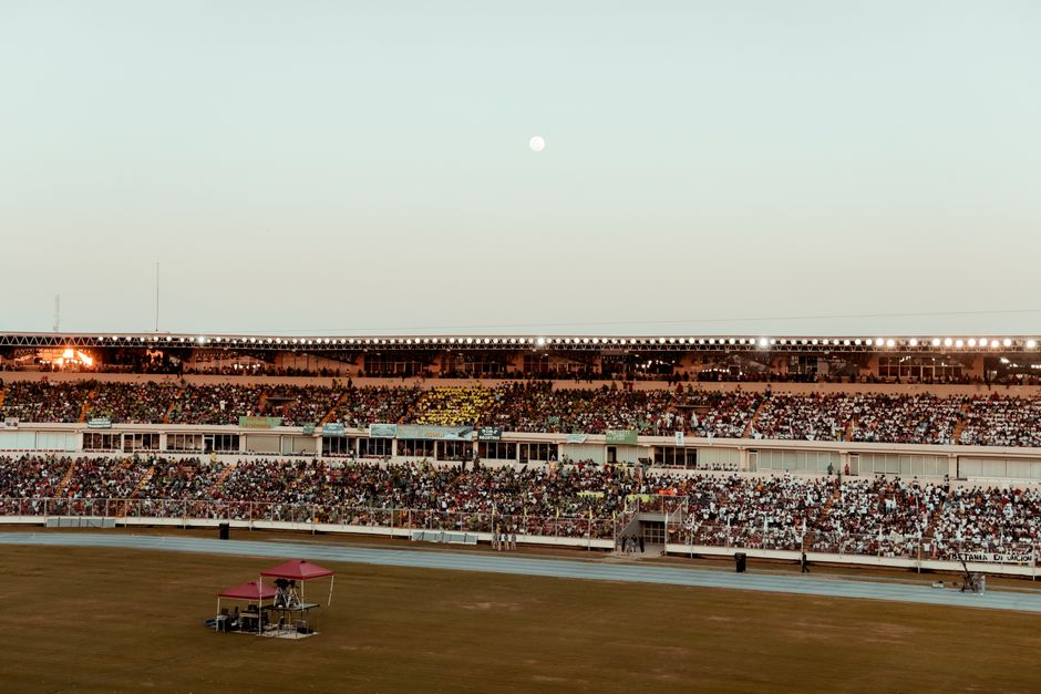 A bustling crowd fills the stadium under a clear evening sky, creating a vibrant atmosphere.