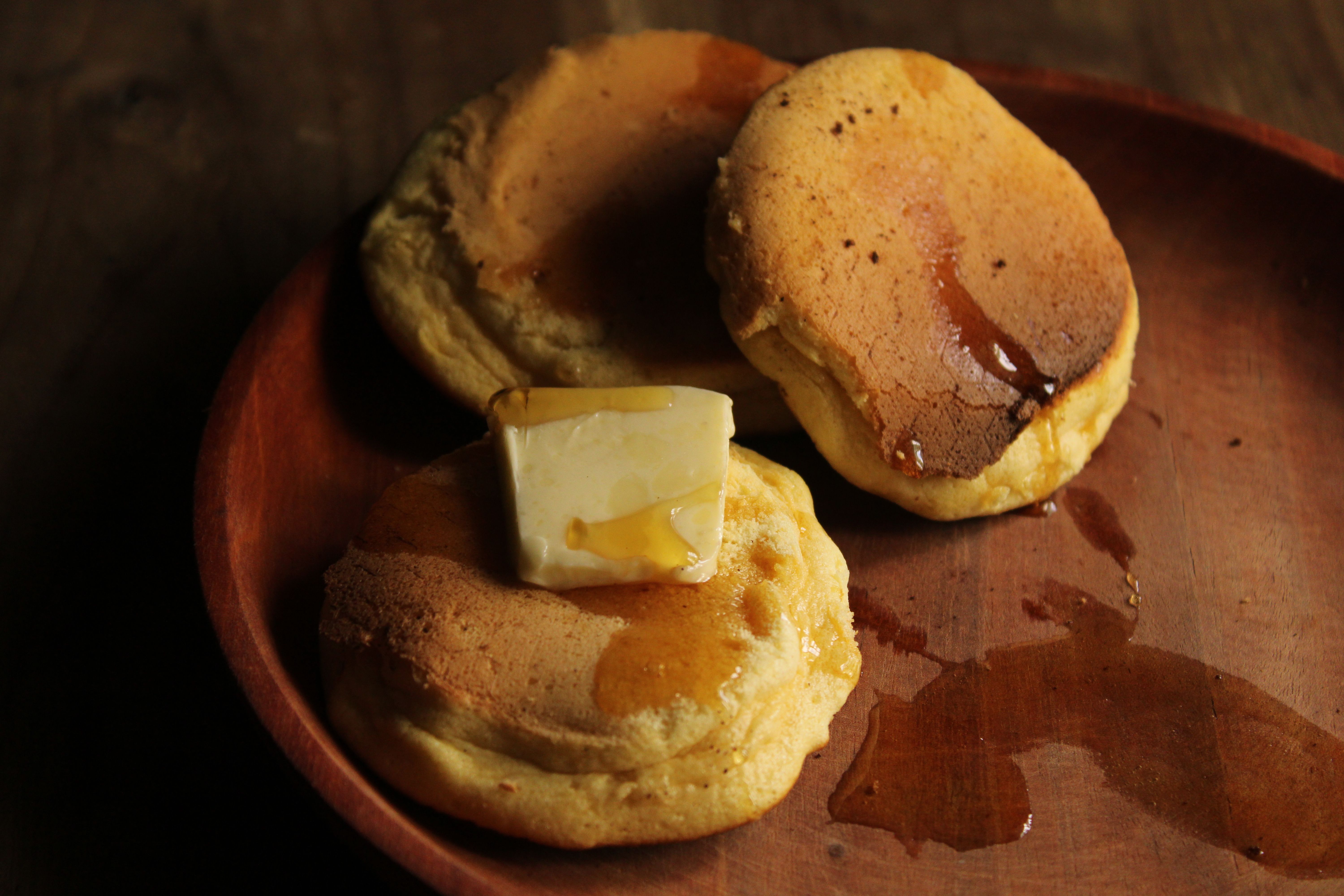 A block of freshly churned pale yellow butter sitting on a wooden board next to a small jar of cloudy buttermilk drained off during churning.